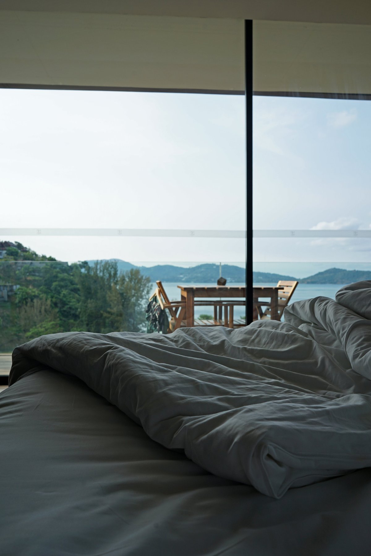 Cozy hotel bed with a terrace patio and a sea view through large glass doors