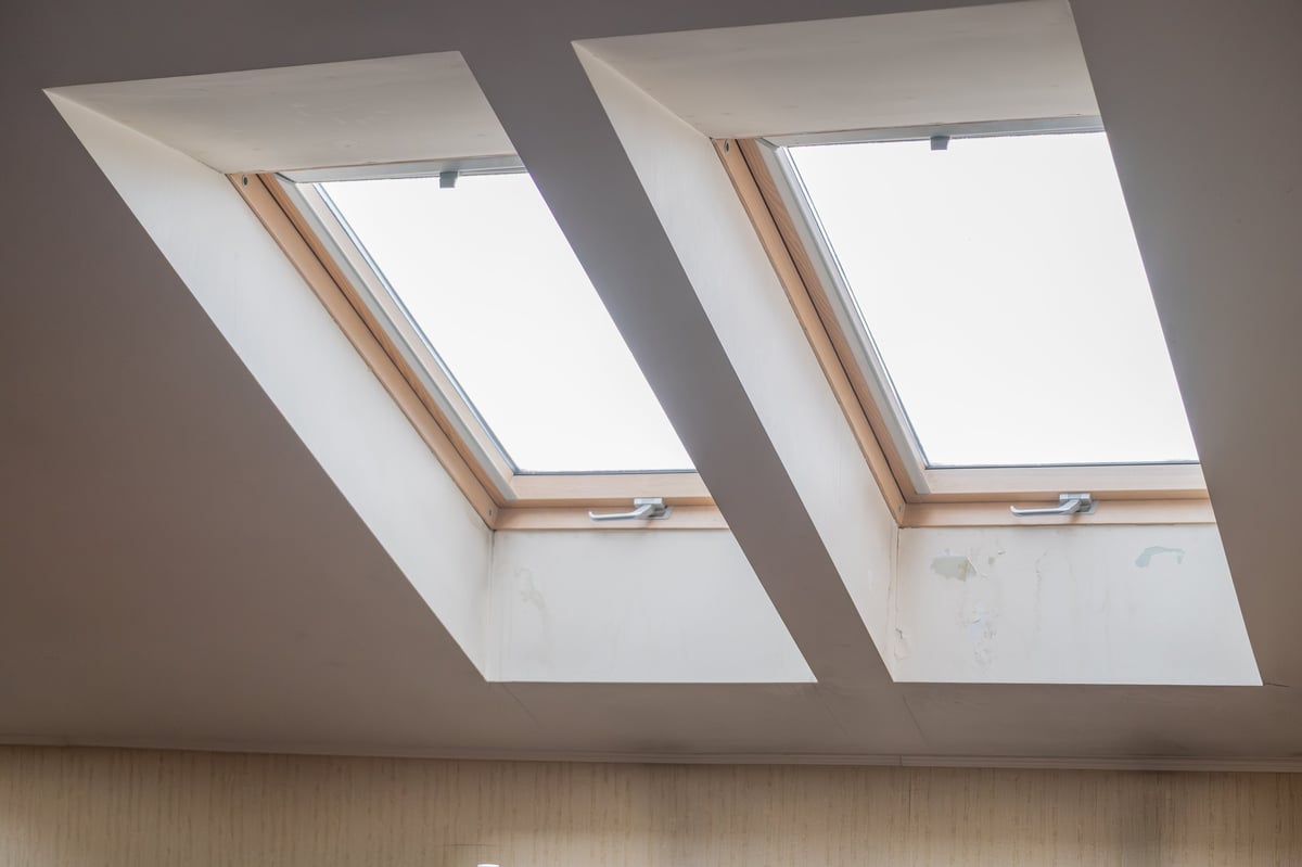 Two modern skylight roof windows installed in sloped ceiling of attic apartment interior. Residential architecture and natural daylight concept with minimalist design and bright indoor atmosphere.