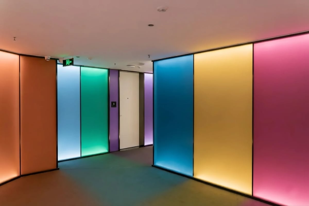 Modern corridor with illuminated colored glass panels in orange, blue, green, yellow, and pink lining both sides of the hallway