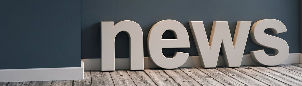 Large 3D grey letters spelling news on a wooden floor against a dark teal wall