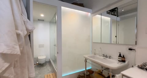Modern bathroom with glass shower enclosure, white sink, large mirror, and wooden floor accents
