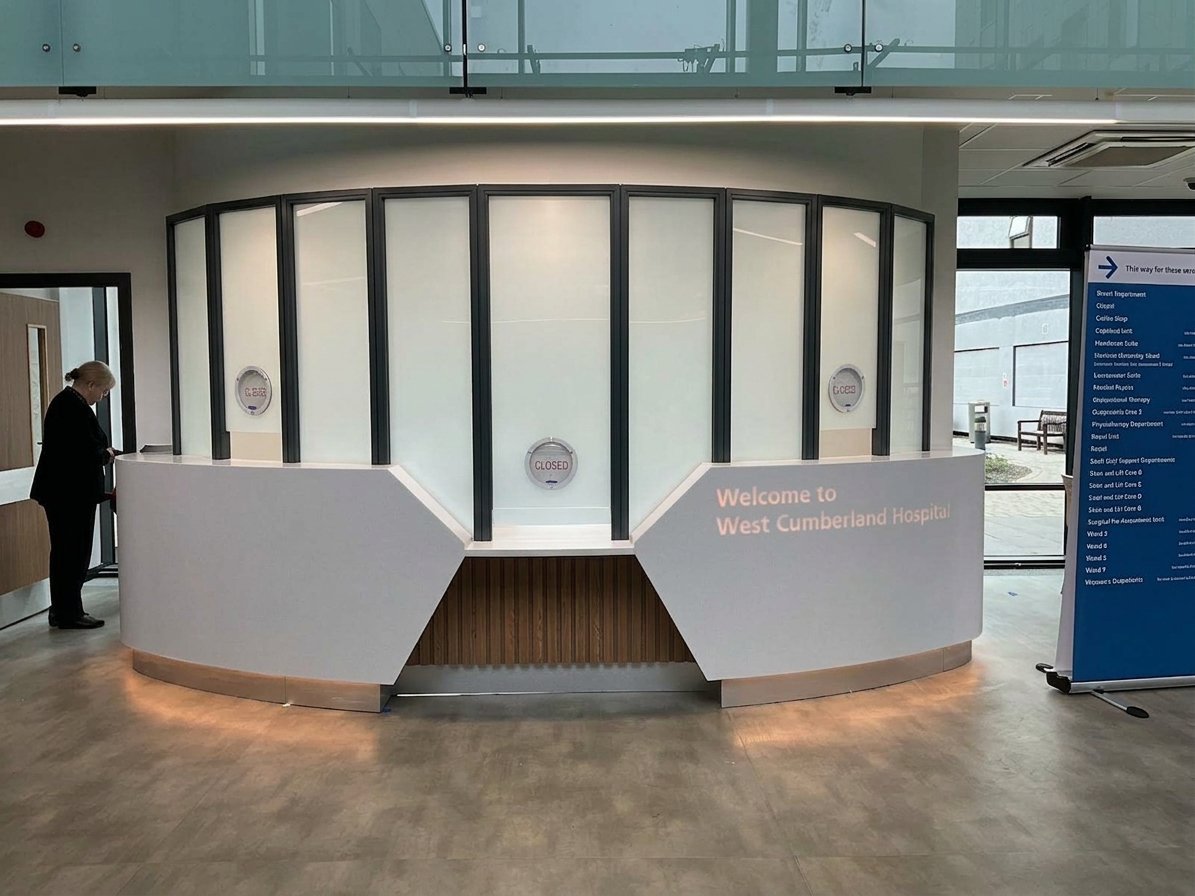 Modern reception desk with curved white countertops and wood paneling in a contemporary office lobby with glass partition walls