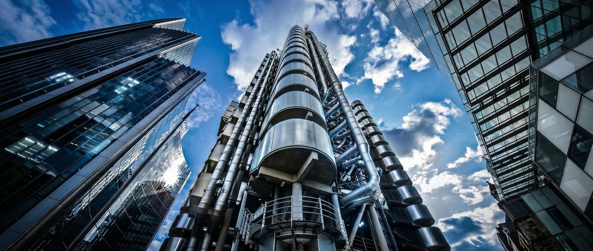 Low-angle view of modern glass and steel skyscrapers against a blue sky with white clouds