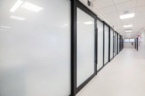 Modern office corridor with frosted glass partitions and black frames lining both sides, bright LED ceiling lights overhead