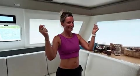 Woman in purple sports top celebrating with thumbs up inside a modern kitchen