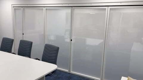 Modern office conference room with frosted glass walls and three black office chairs at a white table