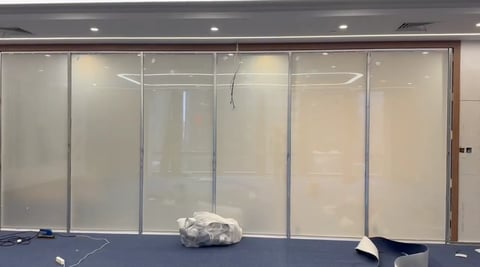 Large glass partition wall with frosted panels in an office or workspace with blue flooring and recessed ceiling lights