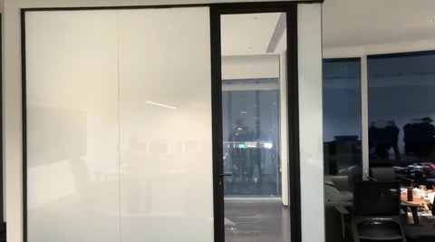 Modern glass sliding doors and windows in an office space with frosted glass panels and dark frames overlooking a city view